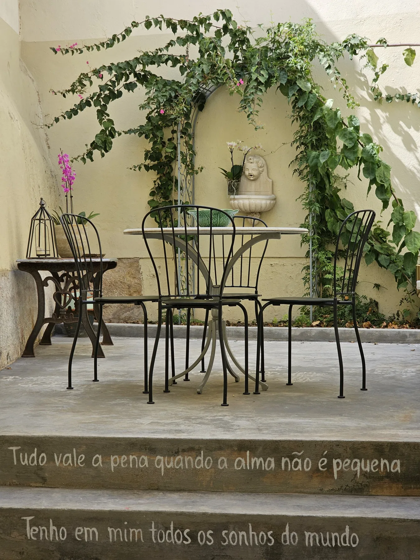 Un patio con asientos bajo enredaderas frondosas y una pequeña fuente en la pared.