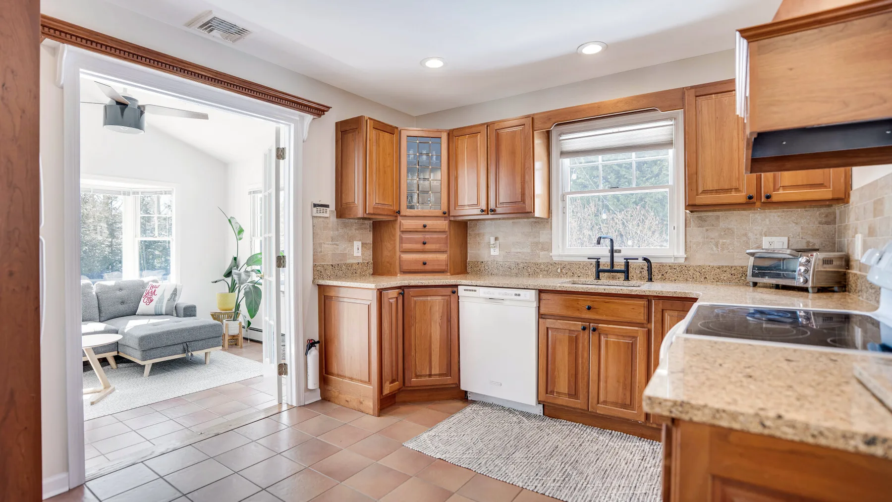 Una cocina con gabinetes de madera, fregadero y lavavajillas junto a una sala de estar abierta.
