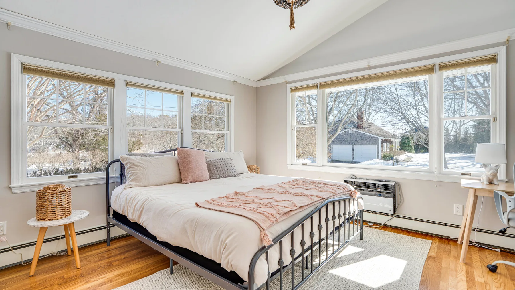 Un dormitorio luminoso con una cama junto a grandes ventanas con vistas a los árboles.