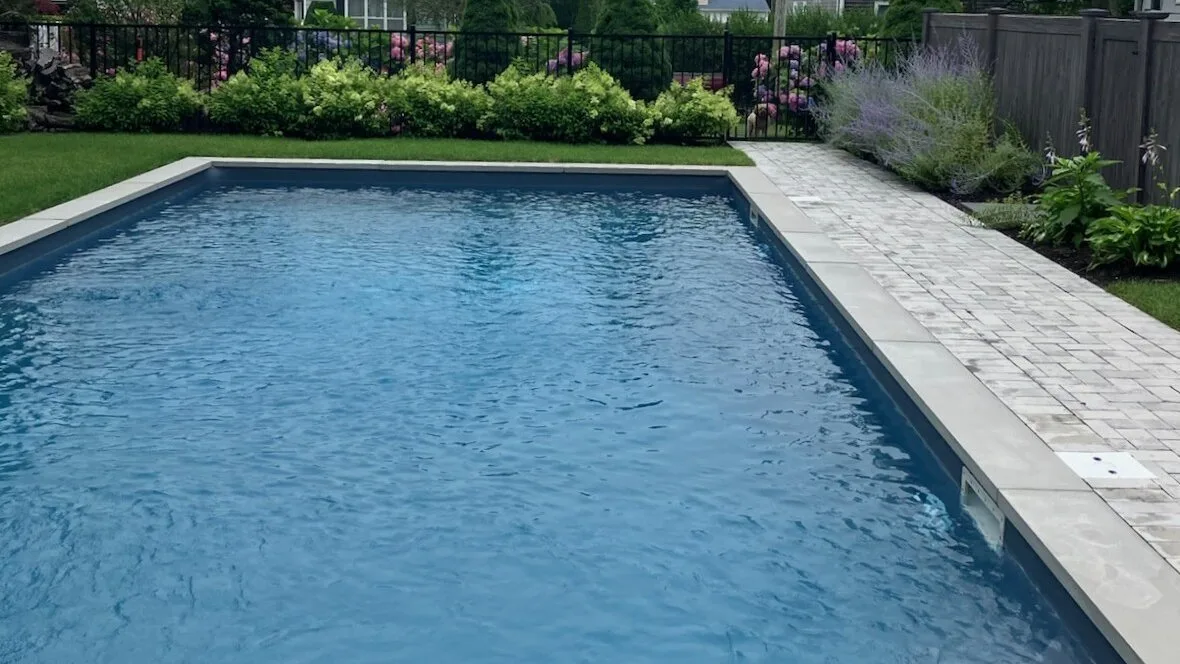 Una piscina en un patio, junto a un sendero pavimentado y plantas.