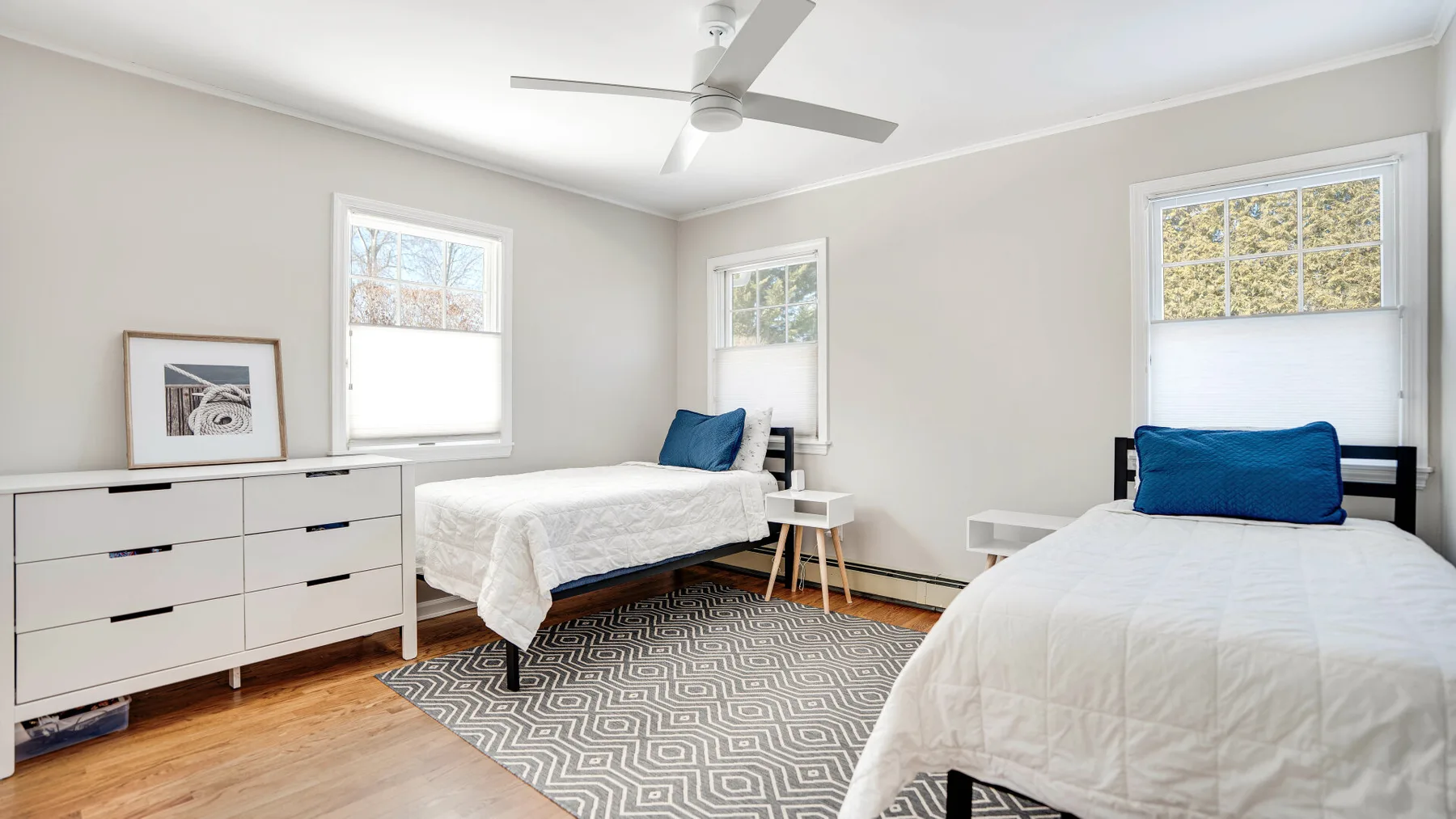 Un dormitorio luminoso con dos camas, ropa de cama blanca y una alfombra estampada.