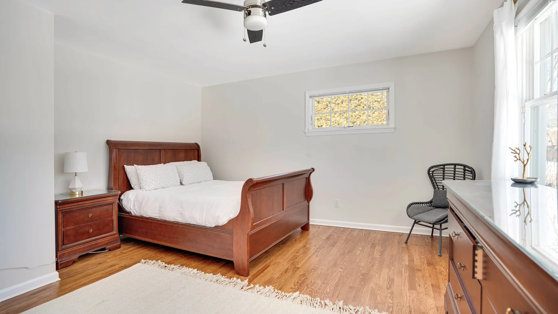 Un dormitorio con una cama de madera, una mesita de noche y ventanas luminosas.