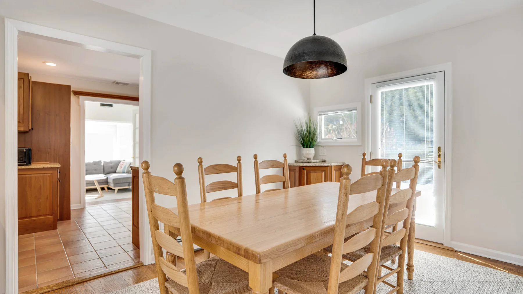 Un comedor luminoso tiene una mesa de madera y sillas bajo una lámpara colgante.
