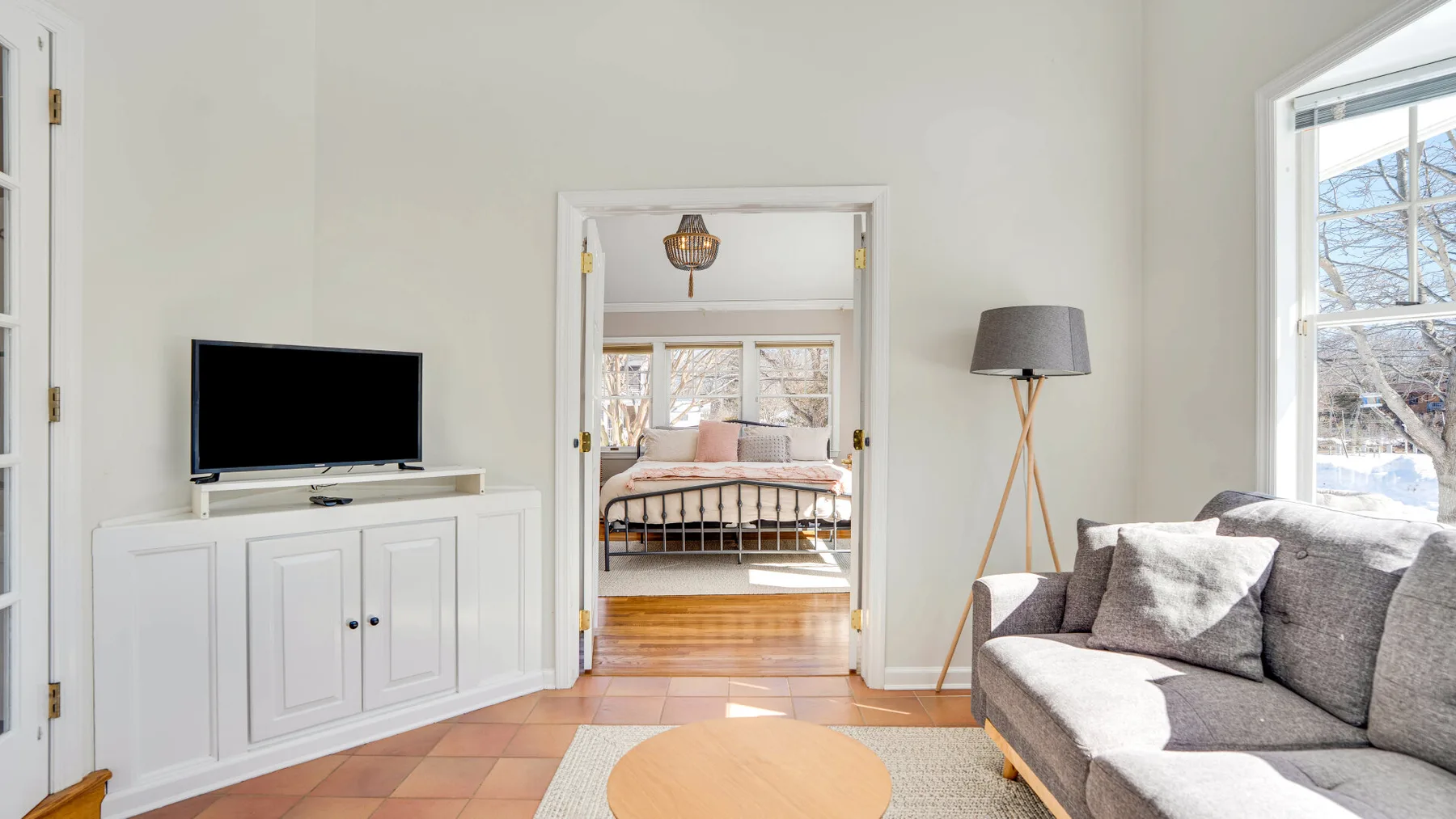 Una sala luminosa tiene un televisor, un mueble blanco y asientos grises.