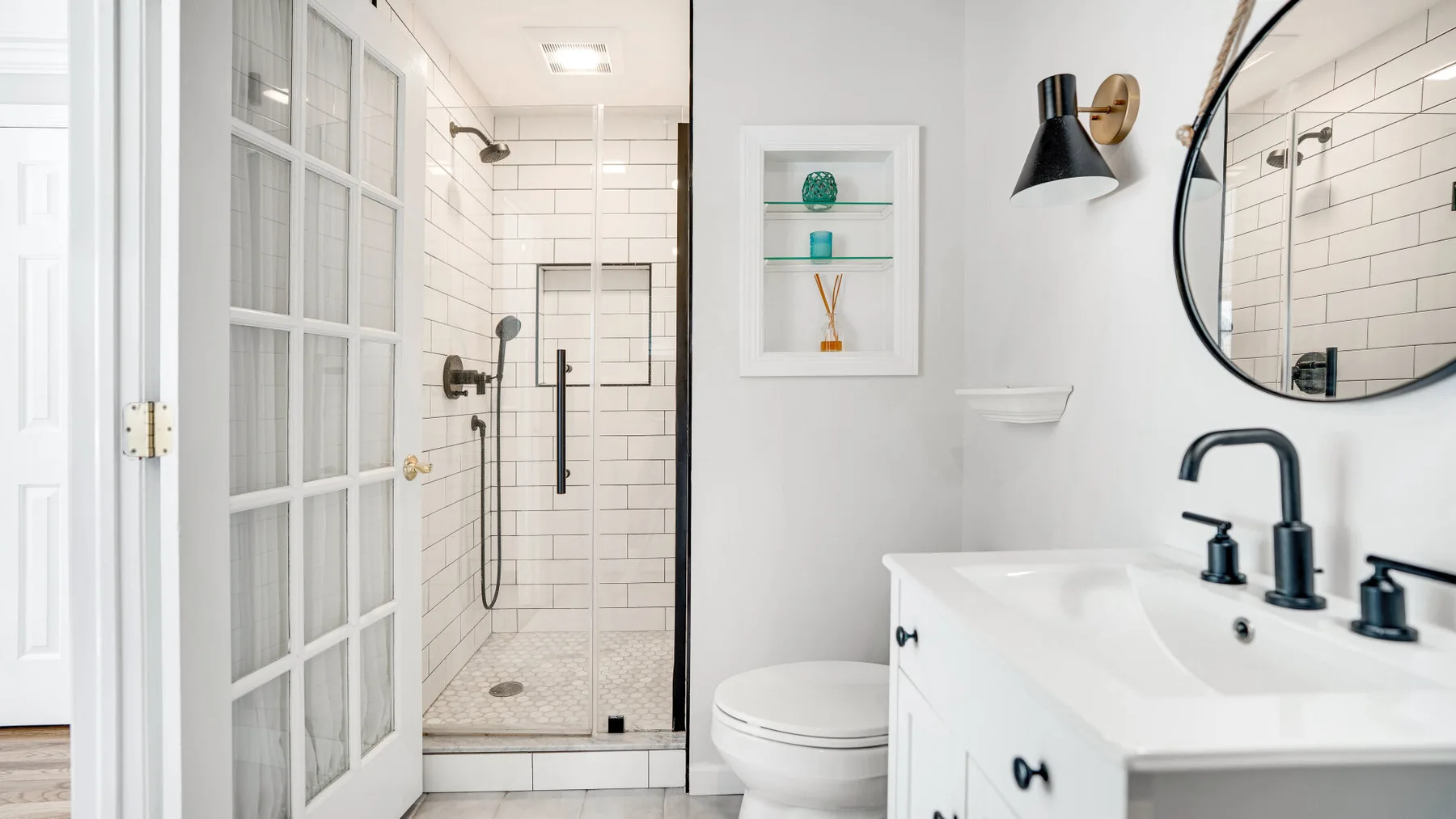 Un baño luminoso con ducha de vidrio, lavabo blanco y espejo redondo.