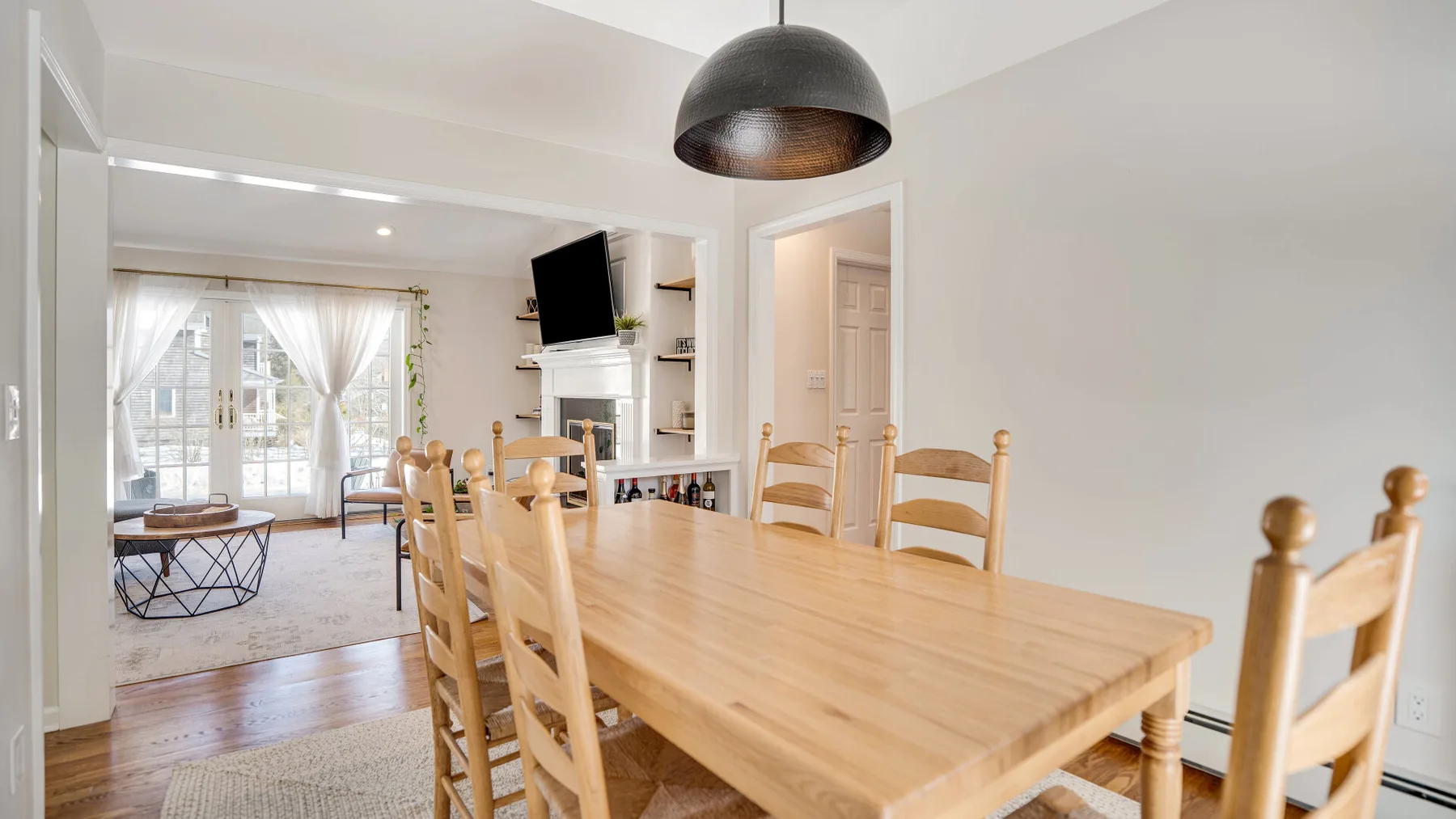 Un comedor con una larga mesa de madera y sillas, abierto a una sala de estar luminosa.