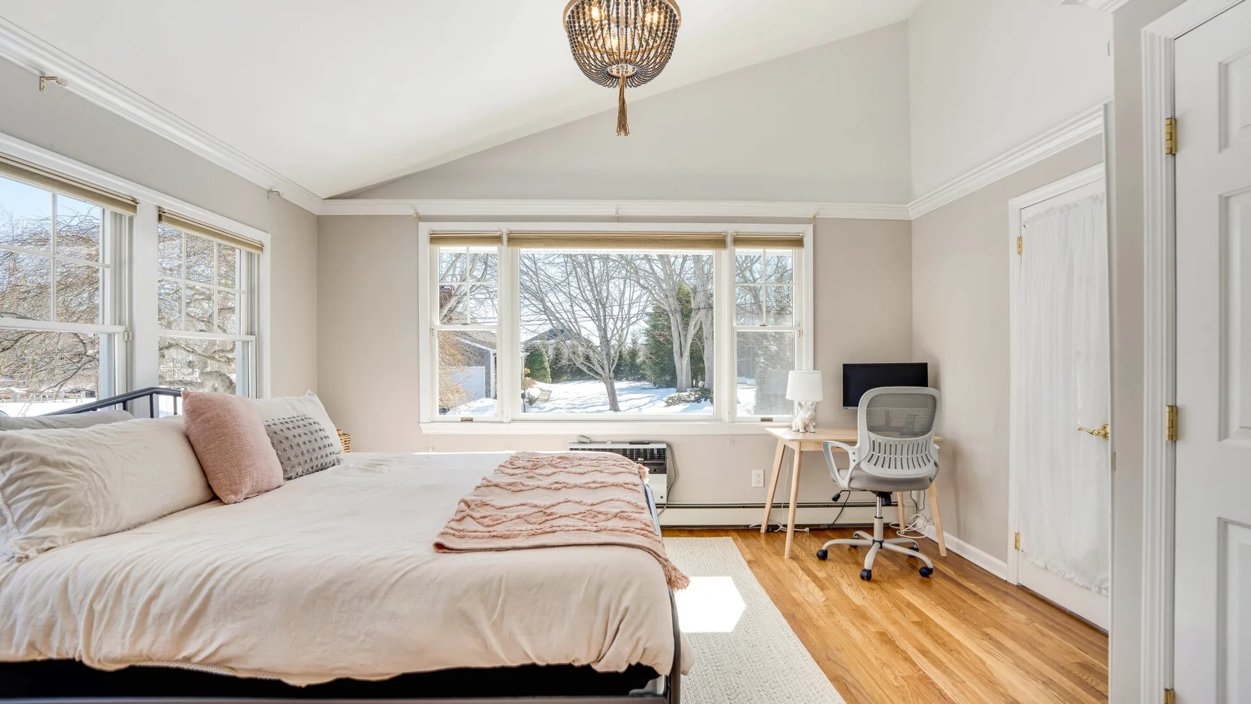 Un dormitorio luminoso con una cama, un escritorio y grandes ventanas con vista a los árboles.