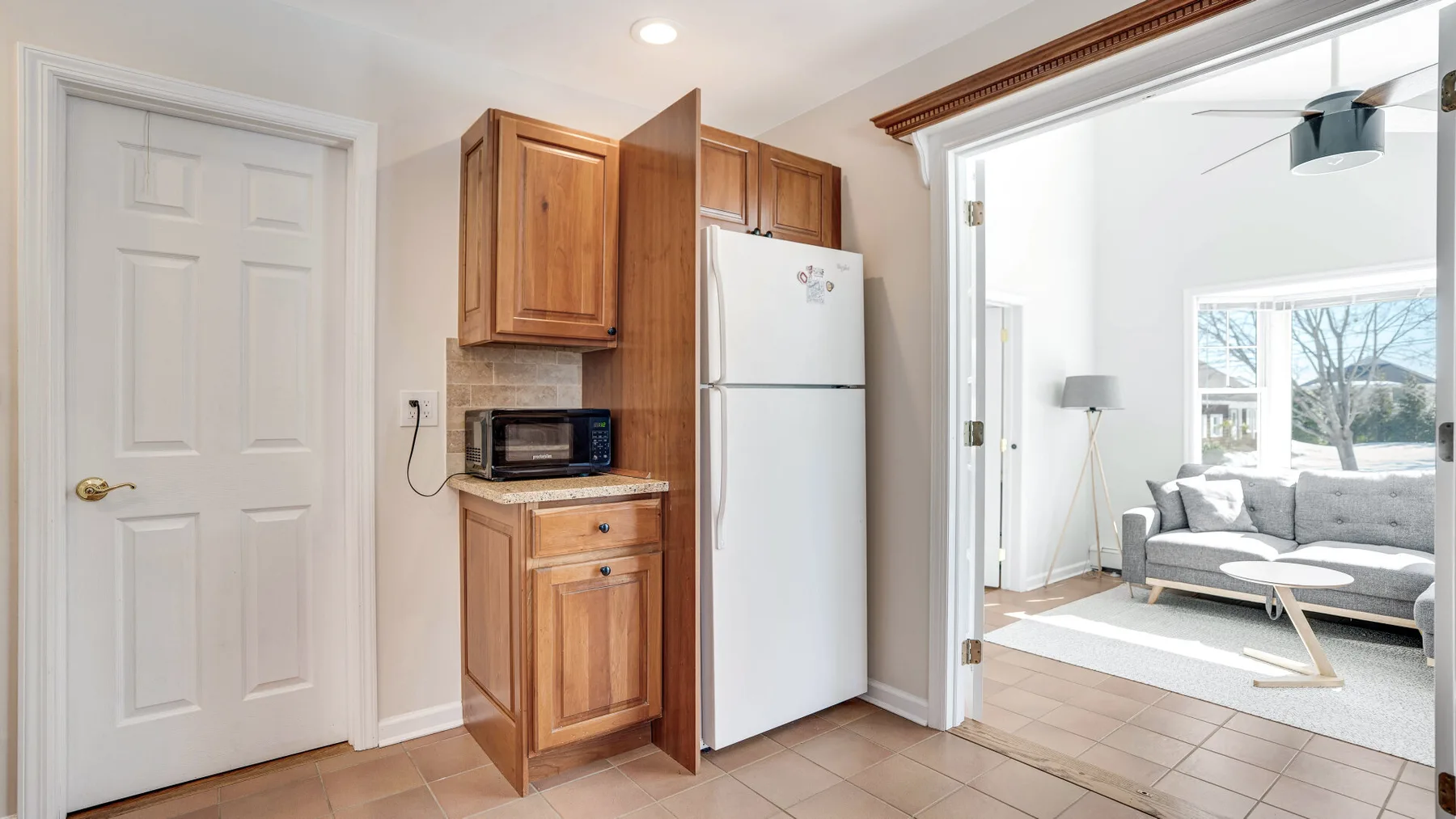 Una pequeña zona de cocina con muebles de madera y un refrigerador blanco junto a una sala de estar.