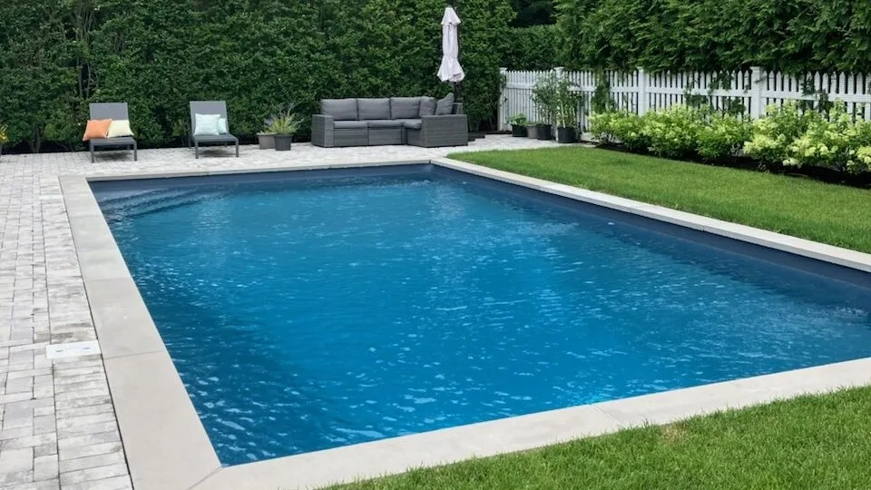 Una piscina exterior está rodeada por una zona pavimentada y césped verde.