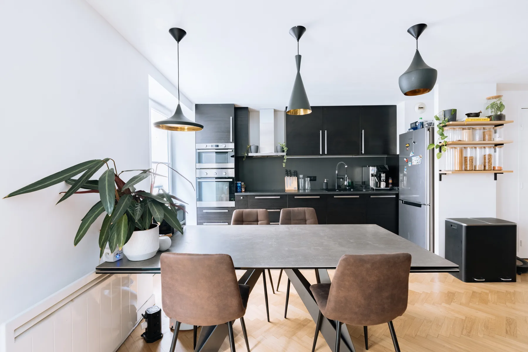 A dining area with a table and seating opens onto a modern kitchen.