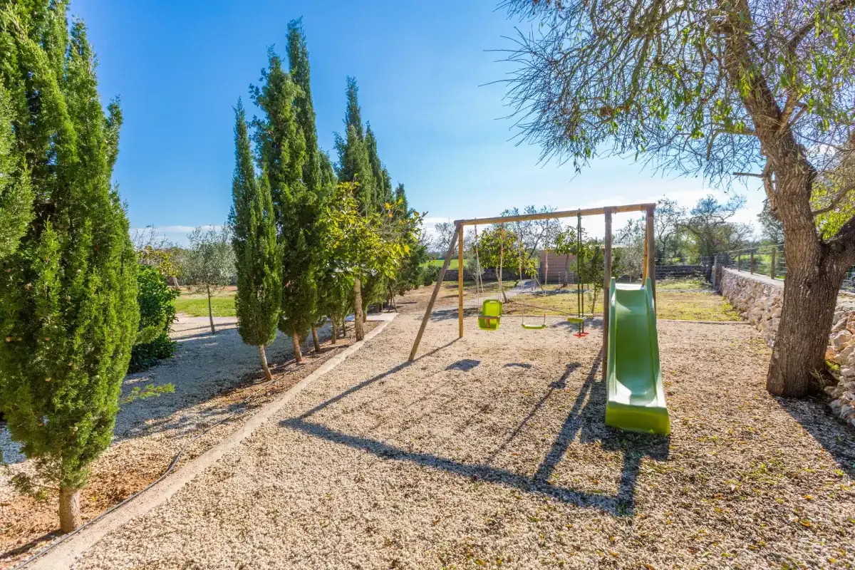 An outdoor playground with a swing set and green slide among trees.