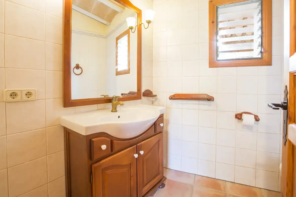 A tiled bathroom with a wooden vanity, mirror, and wall-mounted grab bars.