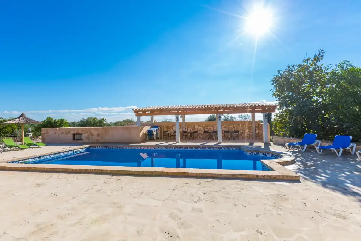 An outdoor swimming pool sits beside a shaded seating area under a sunny sky.