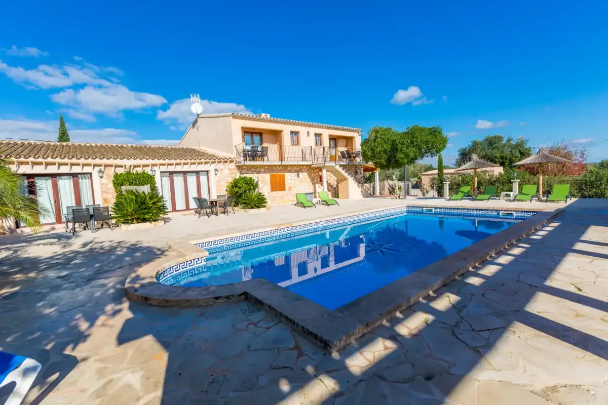 A swimming pool and stone patio sit in front of a sunlit building.