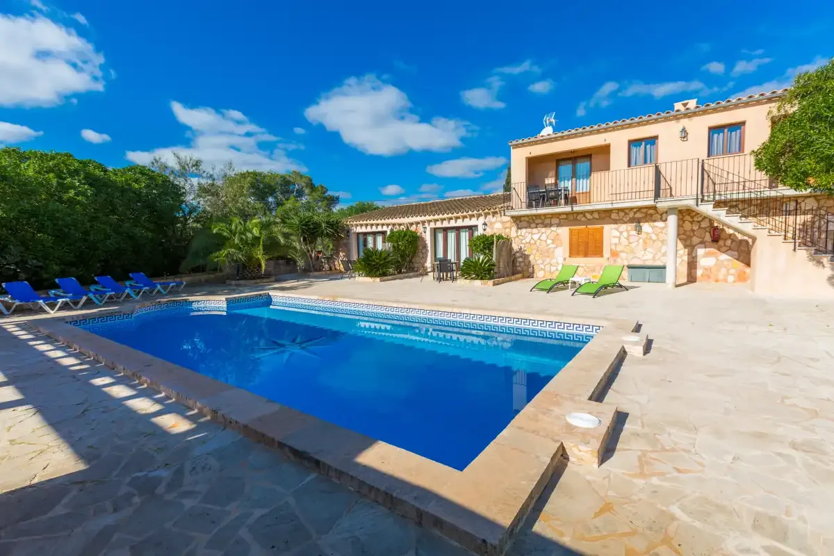 A swimming pool sits beside a stone-clad house and sun loungers.