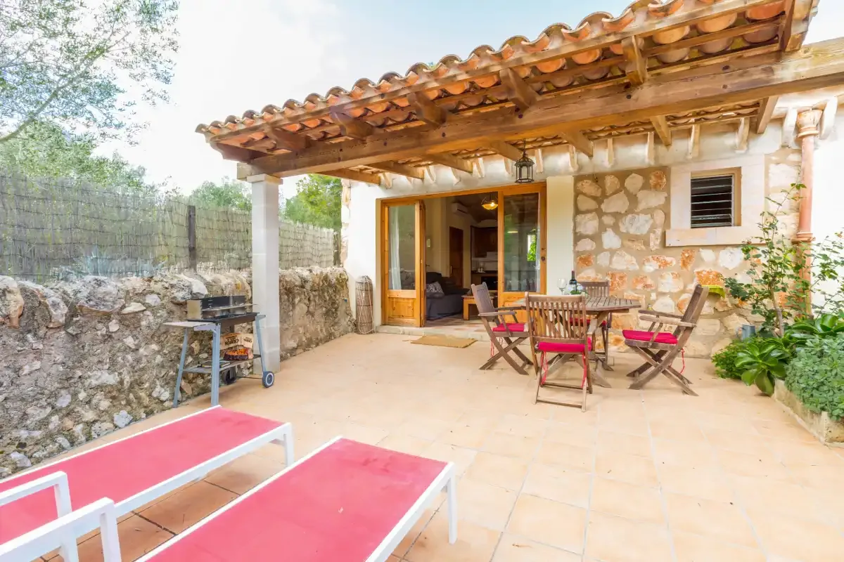 A stone house patio with a wooden pergola and outdoor seating.