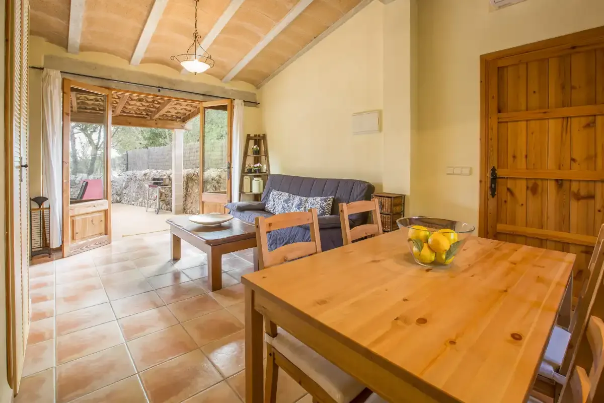 A living and dining area with wooden tables, seating, and doors opening to a patio.
