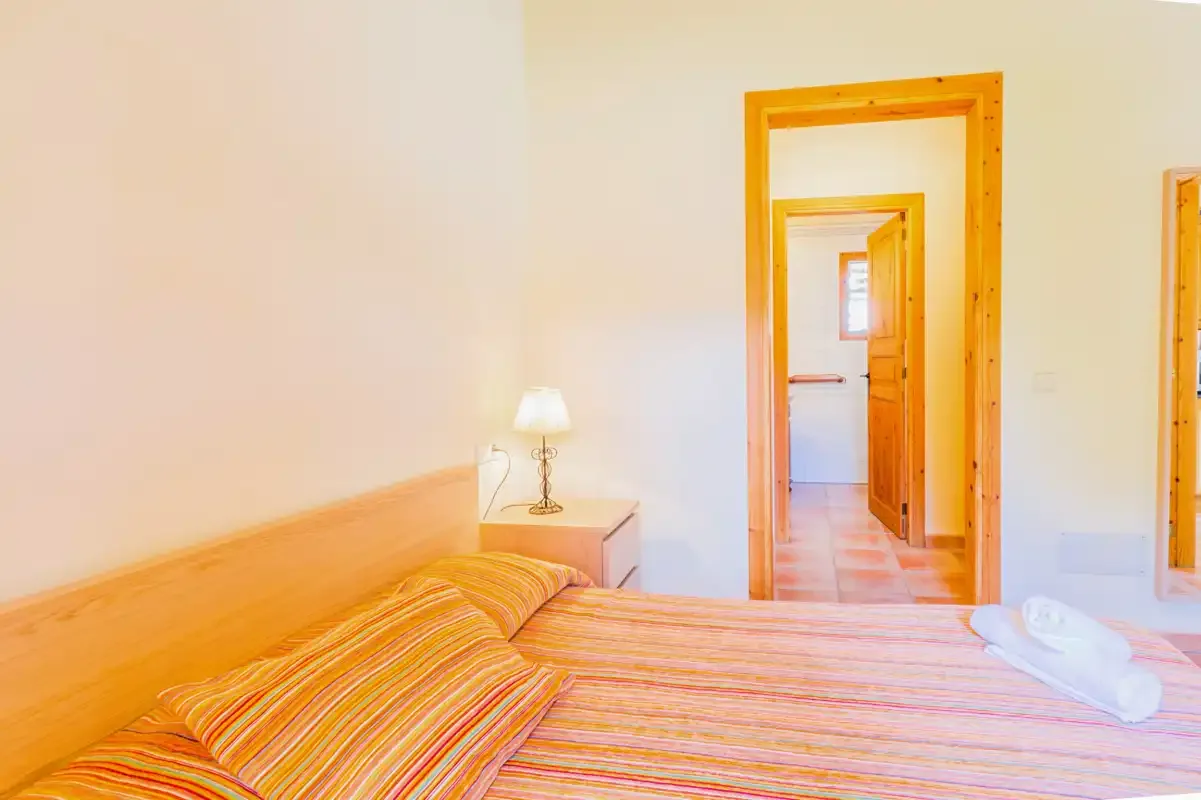 A bedroom with striped bedding and a wooden doorway opening onto a hallway.