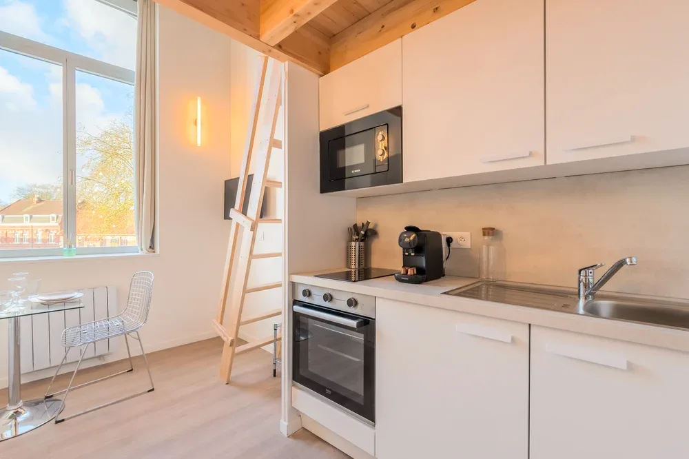A bright kitchen with white cabinetry, an oven, and a counter beside a large window.
