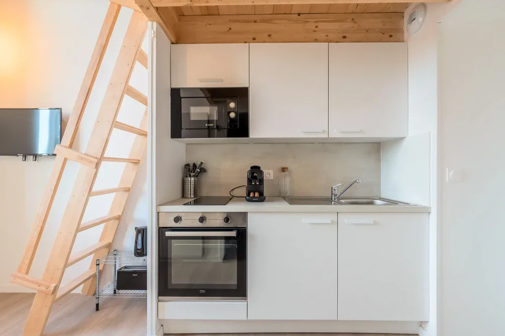 A compact kitchen with white cabinets, a countertop, and built-in appliances.