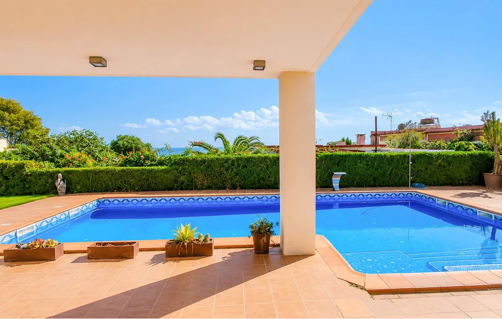 A swimming pool sits beside a tiled patio, with greenery along the edge.