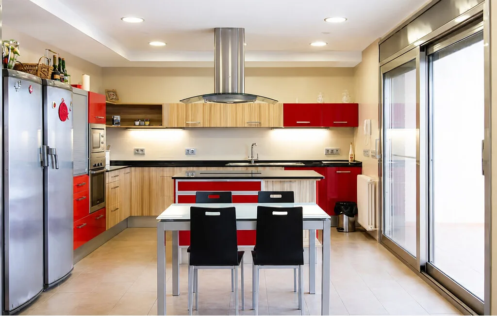 A modern kitchen with a central dining table and large glass doors.