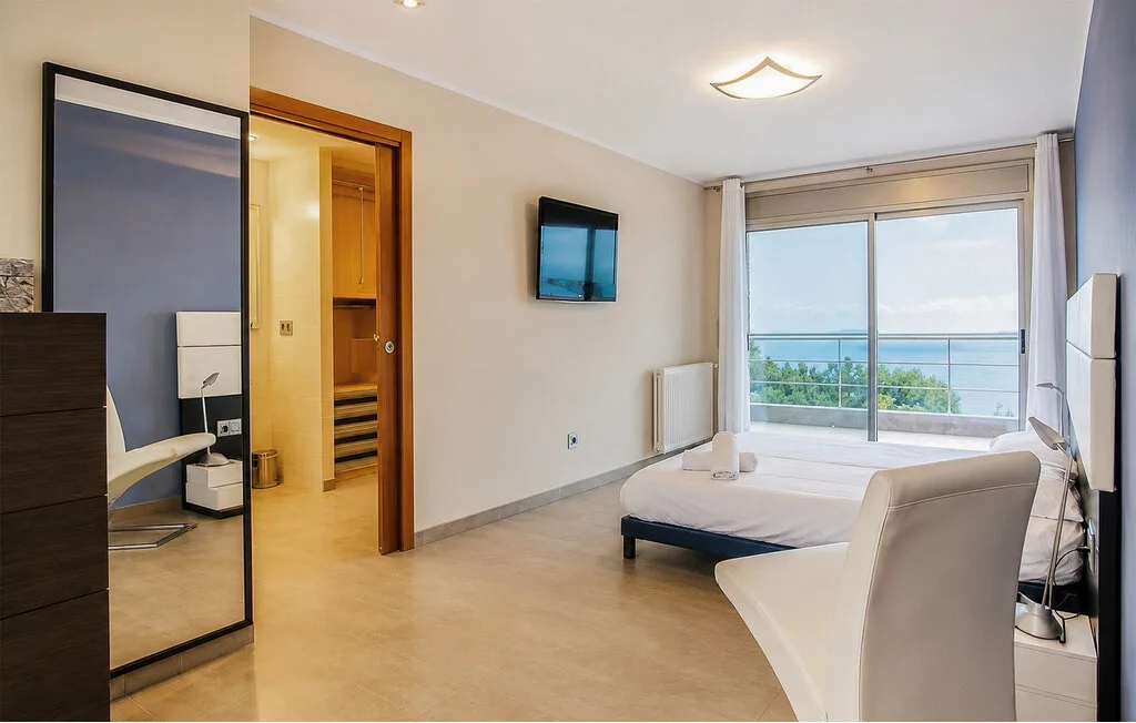 A bedroom with a bed, a television, and sliding glass doors opening to a balcony.