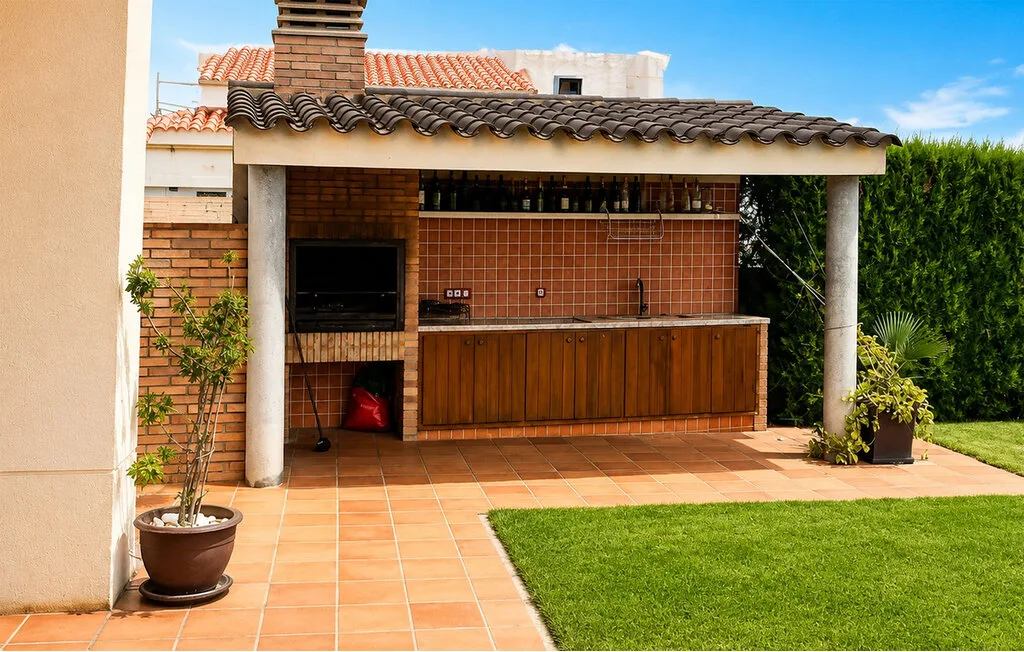 Una zona de barbacoa al aire libre con una encimera de azulejos junto a un jardín con césped.