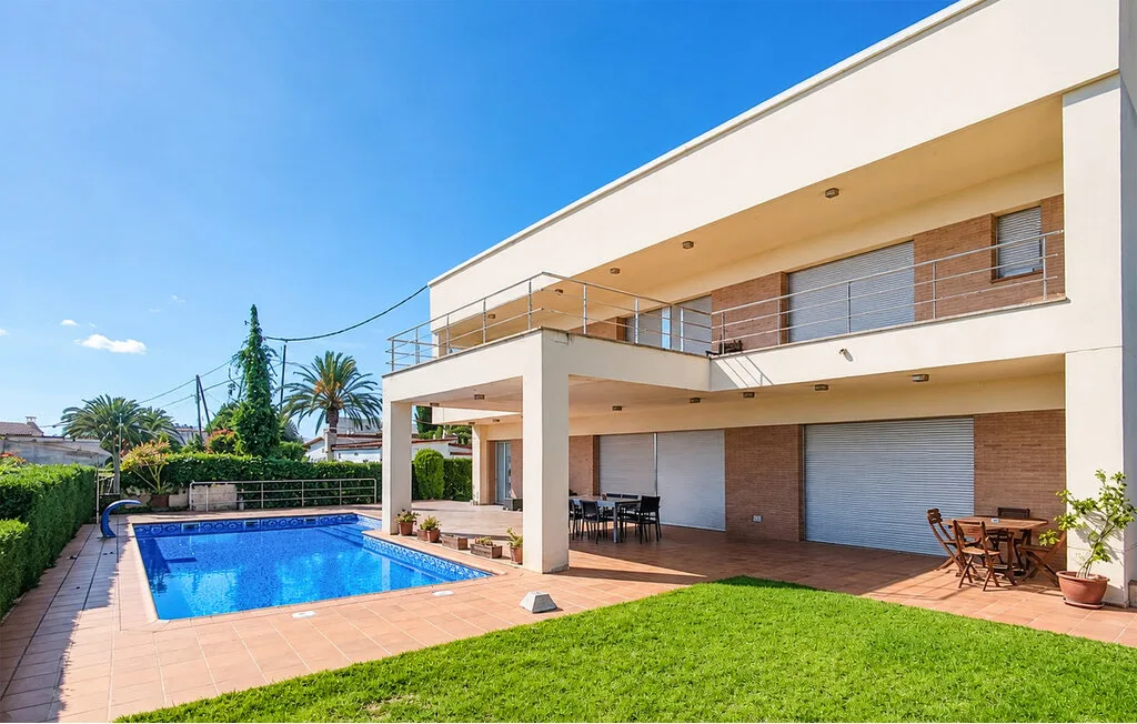 A modern house opens onto a swimming pool and a lawn under a clear blue sky.