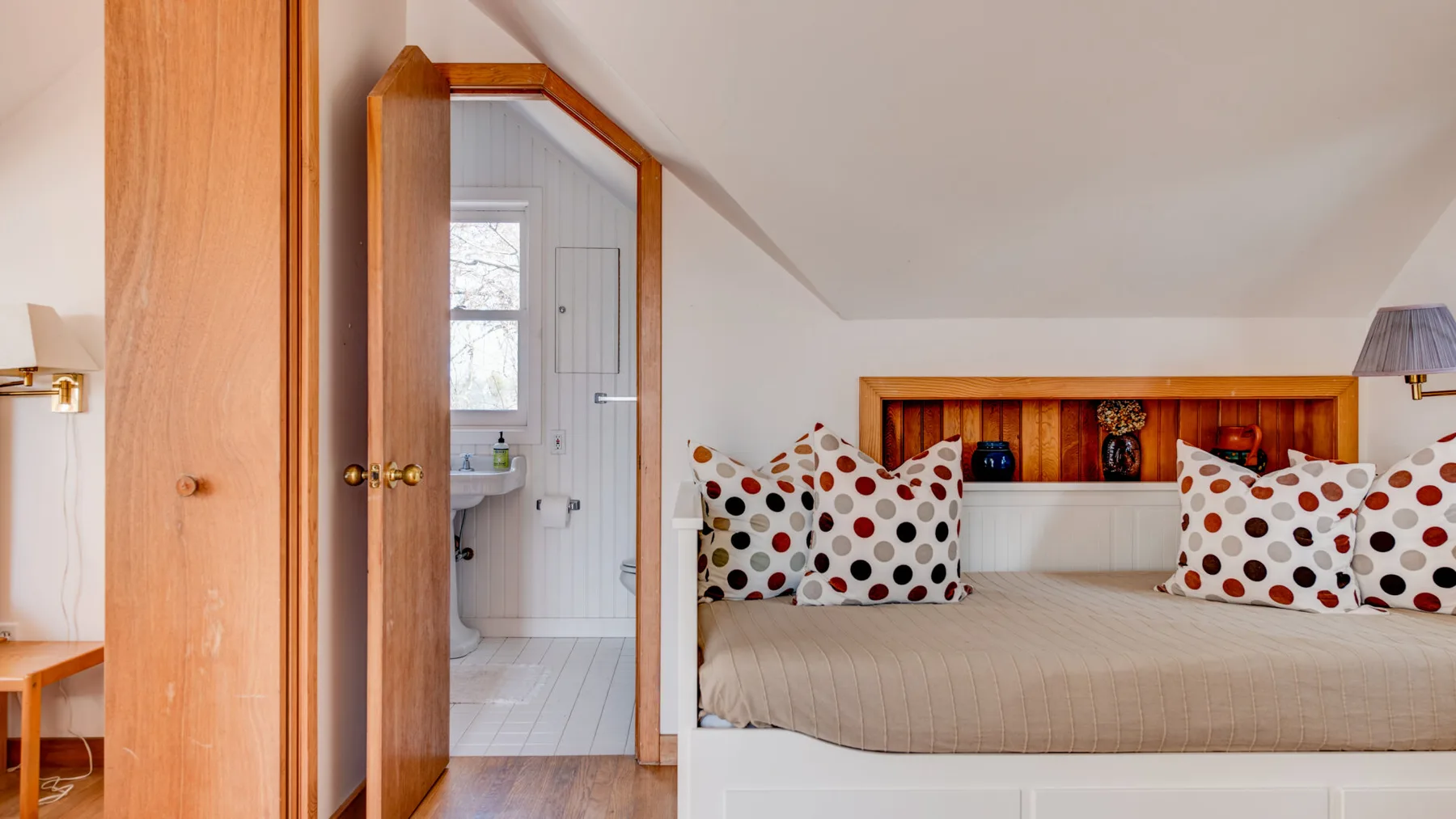 A bedroom with a bed beneath a sloped ceiling and an adjoining bathroom.