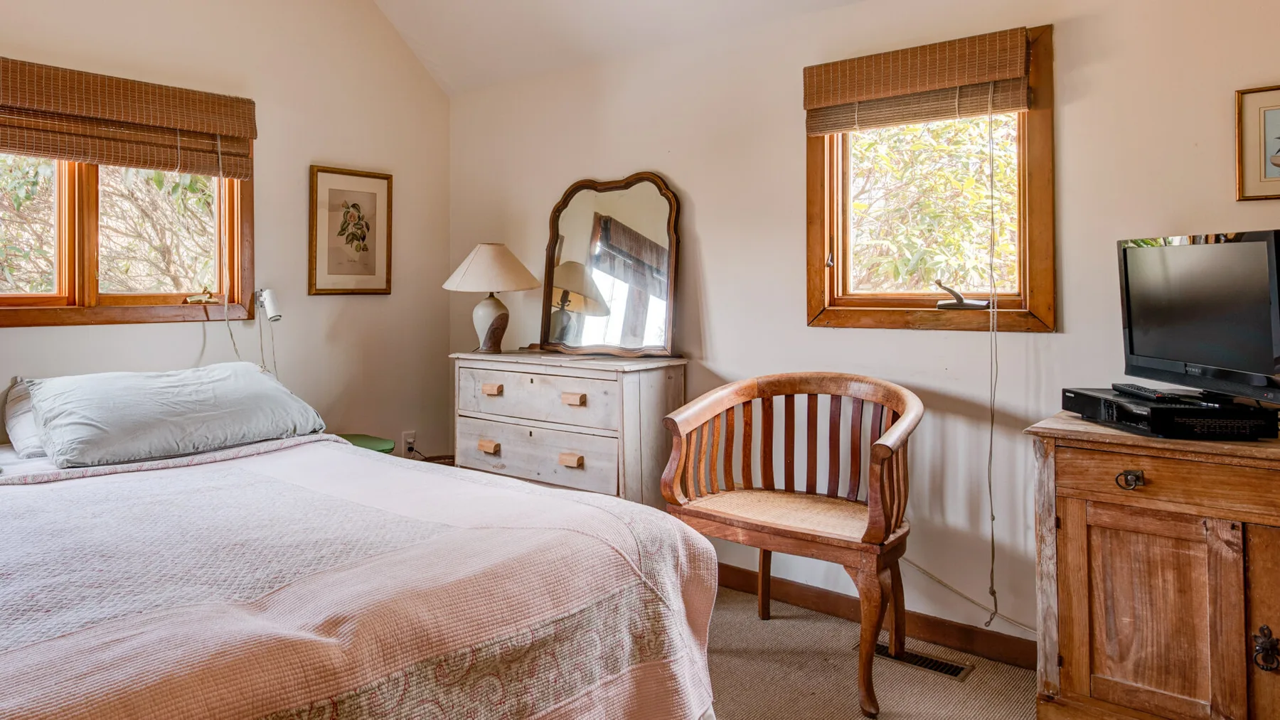 A bedroom with a bed, a wooden chair, and two windows.