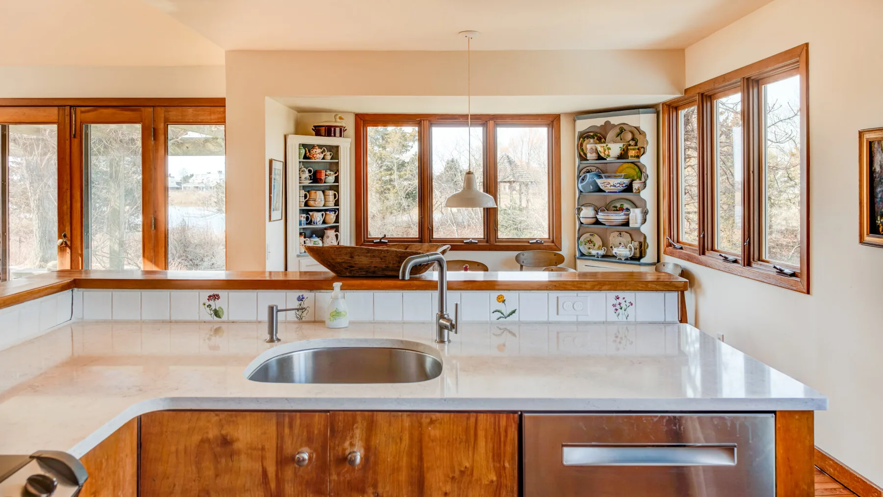 A bright kitchen with a sink and broad windows overlooking trees.