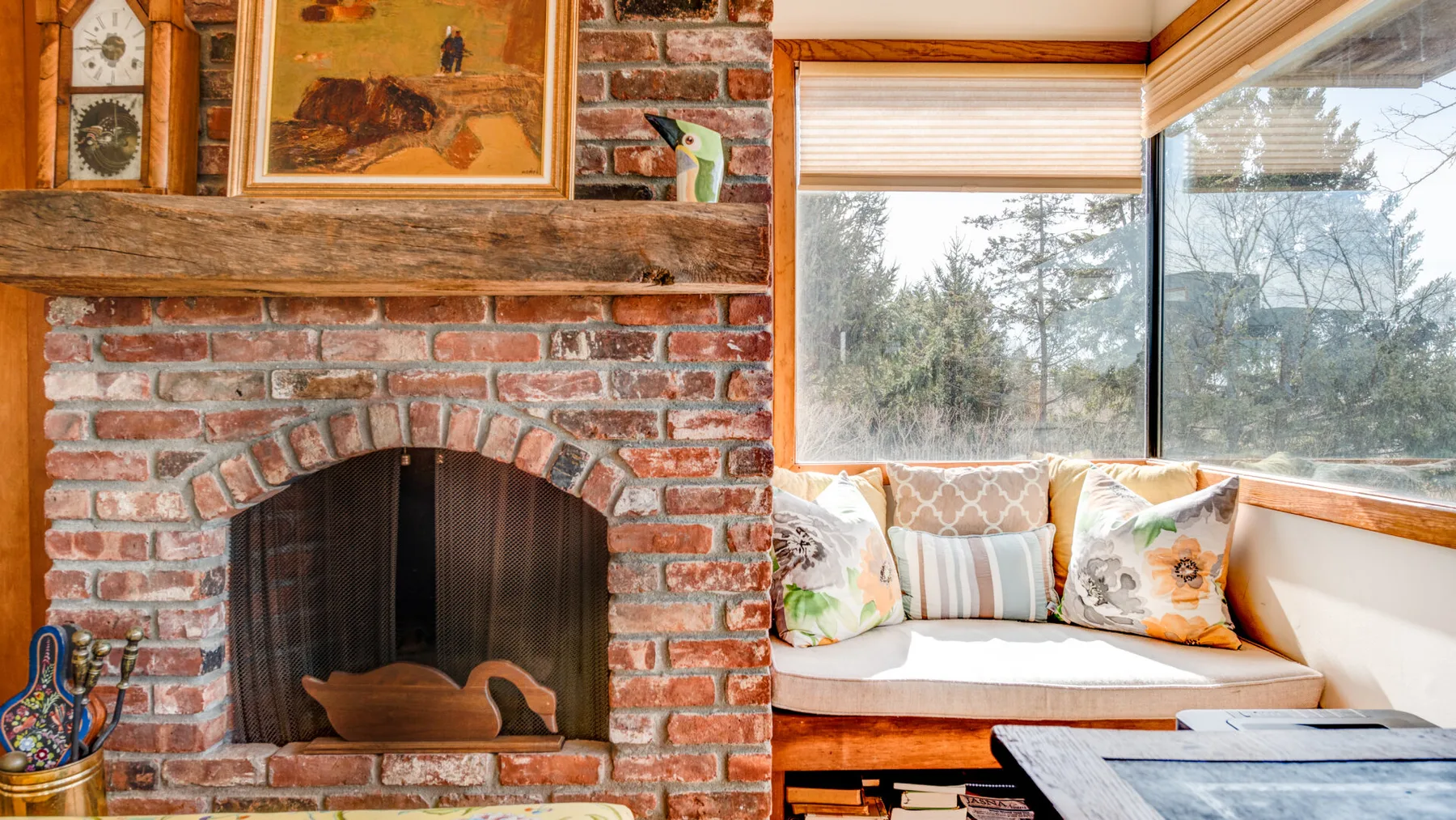 A brick fireplace sits beside a window seating area with cushions.