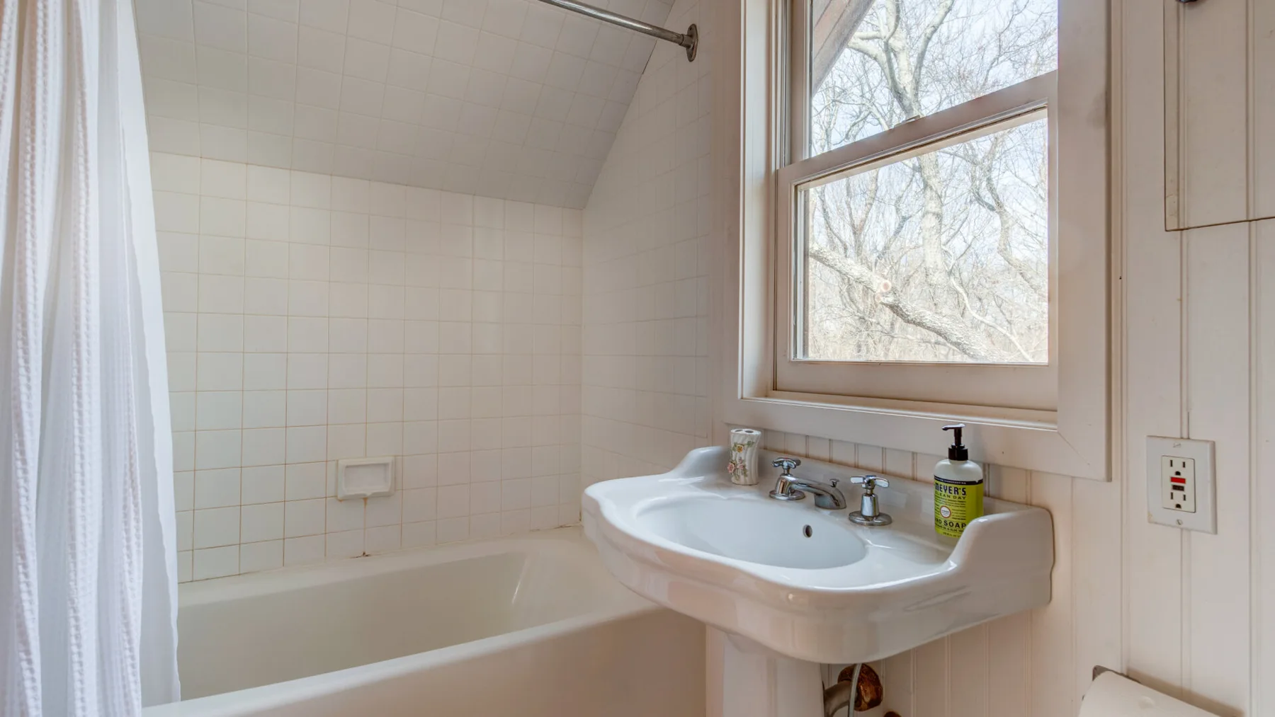 A bathroom with a bathtub, shower curtain, and sink beside a window.