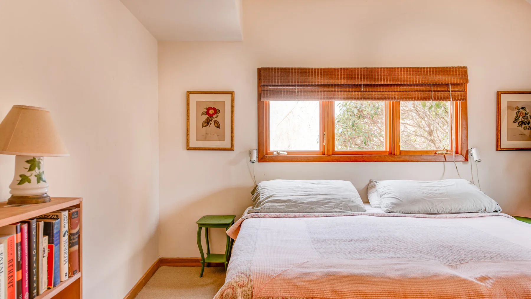 A bedroom with two beds beneath a wide window and wooden blinds.