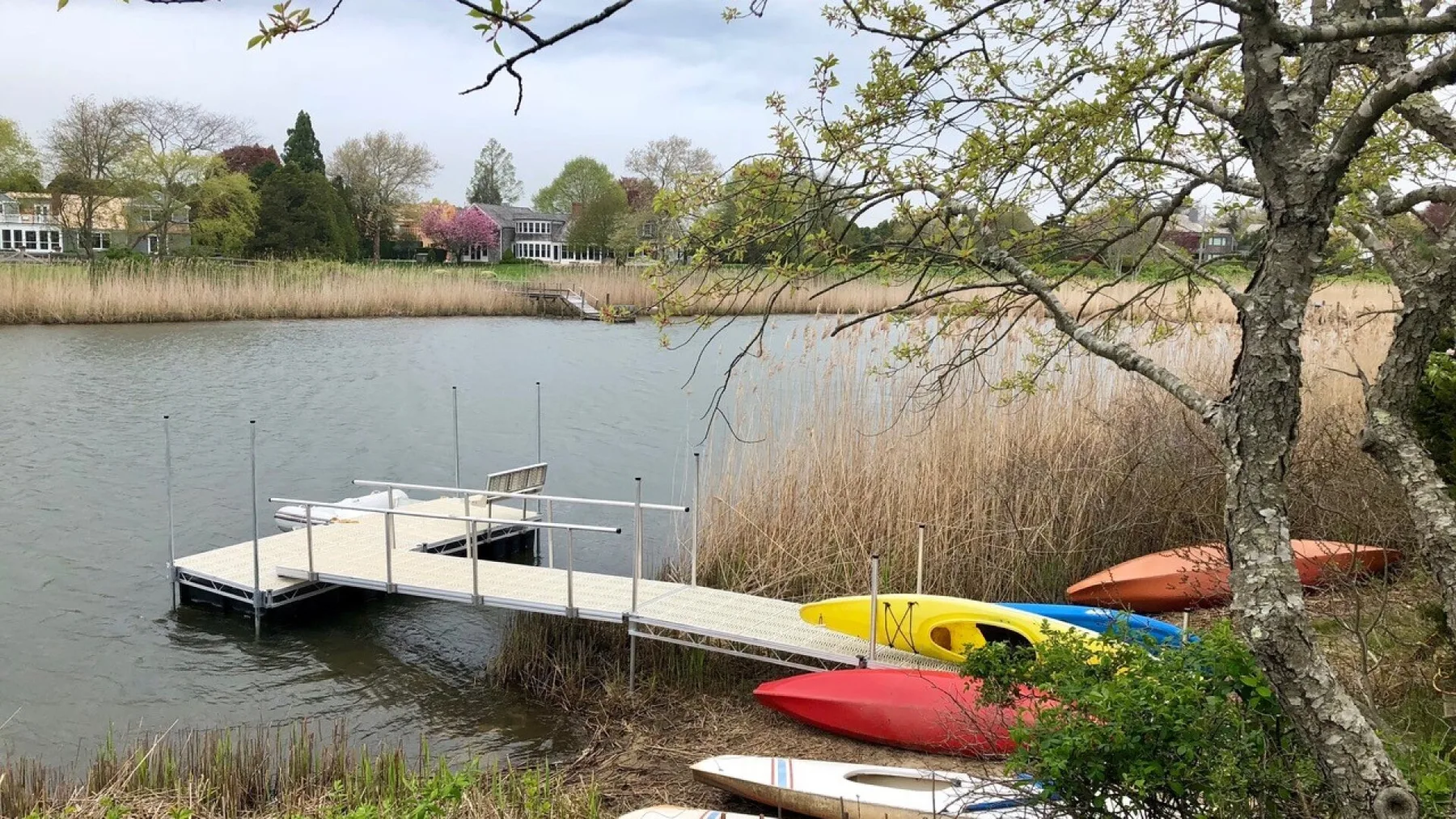A lakeside dock extends over the water beside reeds and colorful kayaks.