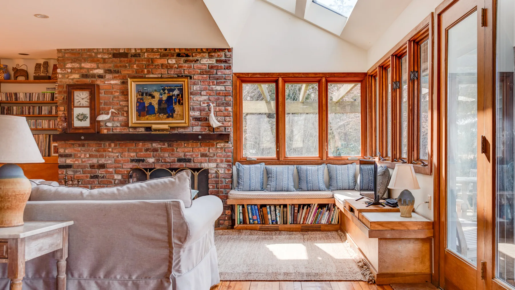 A bright sitting room with cushioned seating, a brick fireplace, and large windows.