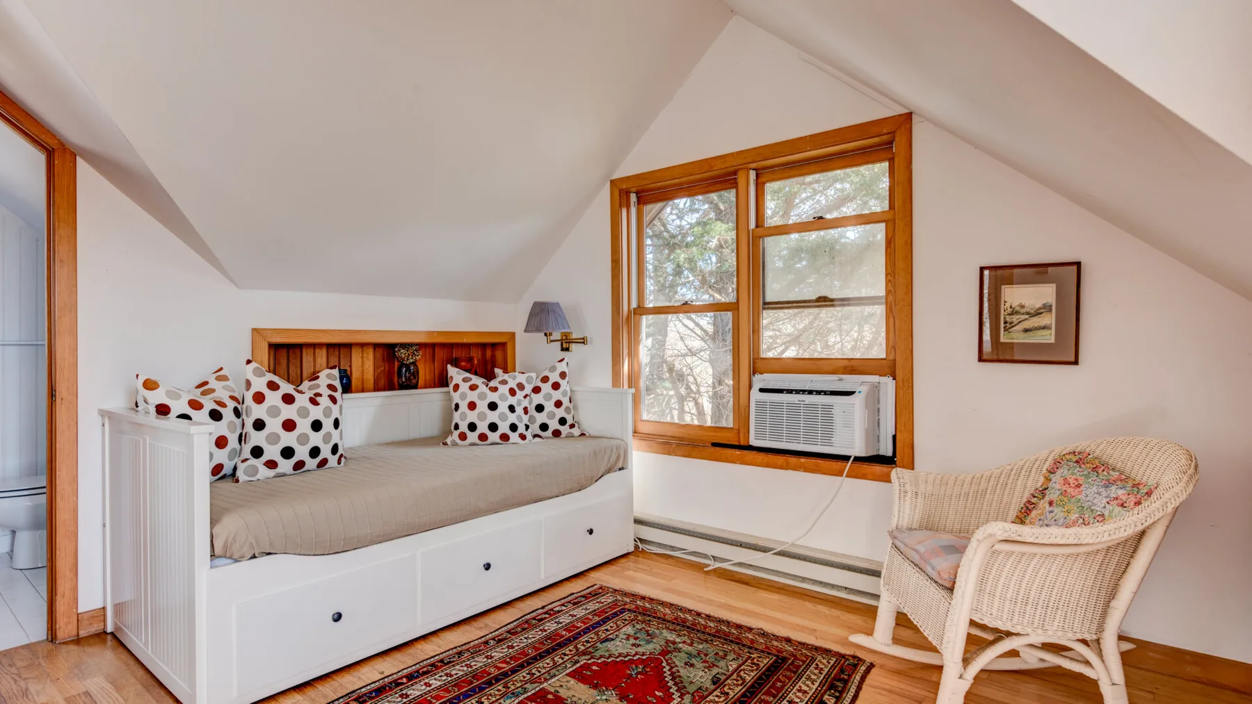 A bright attic bedroom with a white daybed, patterned cushions, and a window.