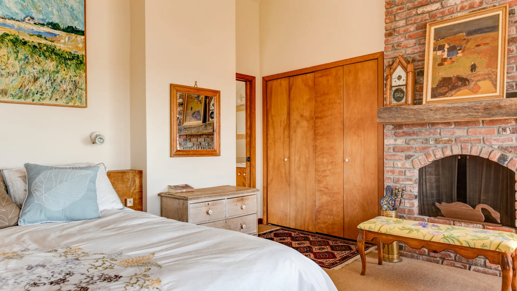 A bedroom with a bed, wooden wardrobe, and brick fireplace.