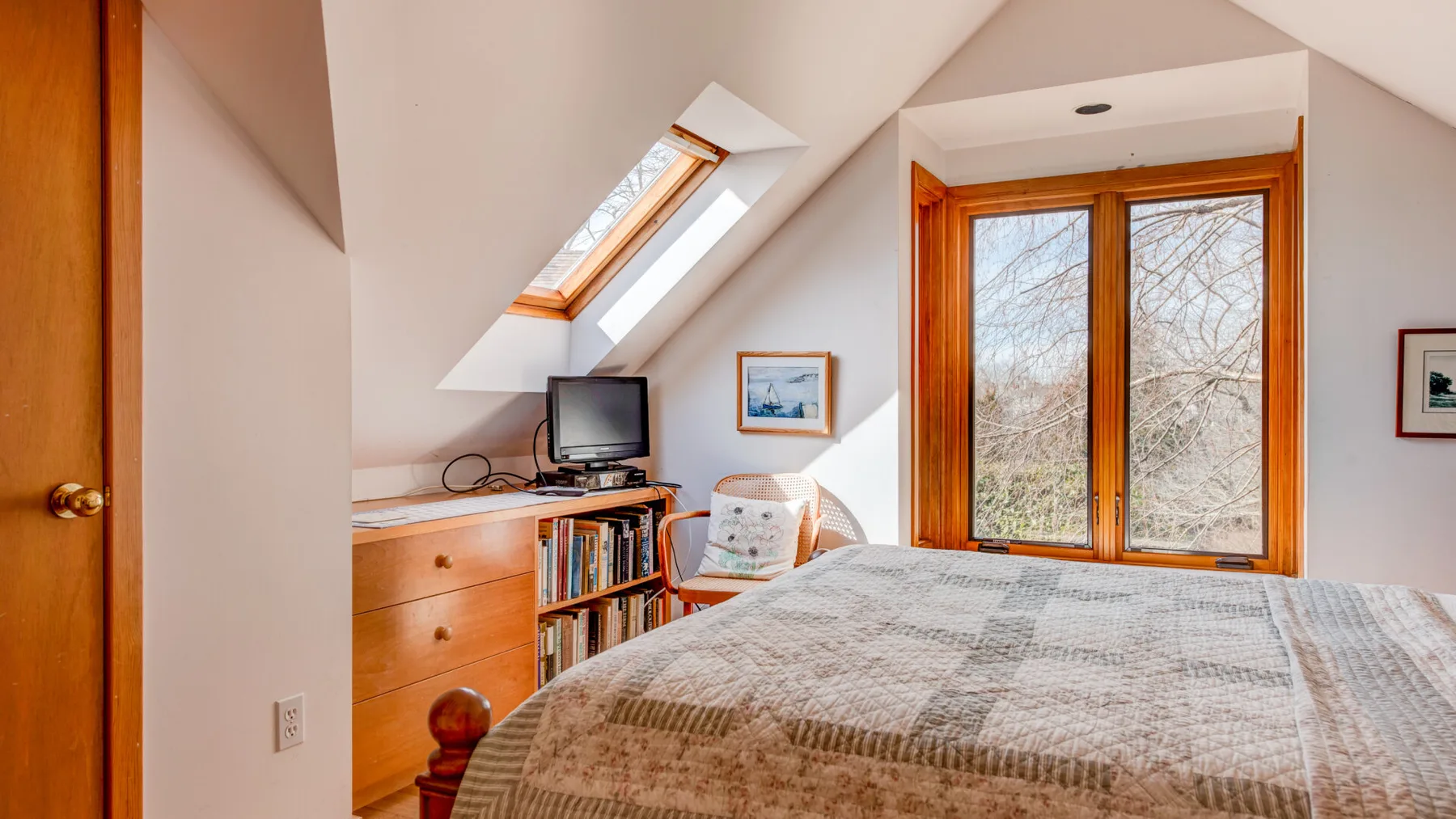 A bedroom with a bed beneath sloped ceilings and a large window.