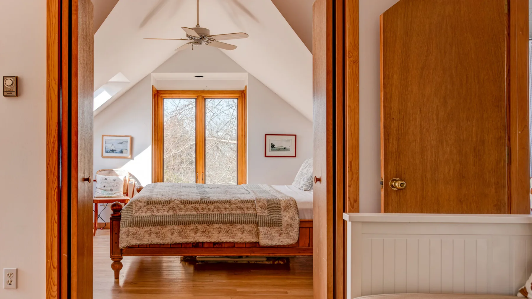 A bedroom with a bed beneath a sloped ceiling and a large window.