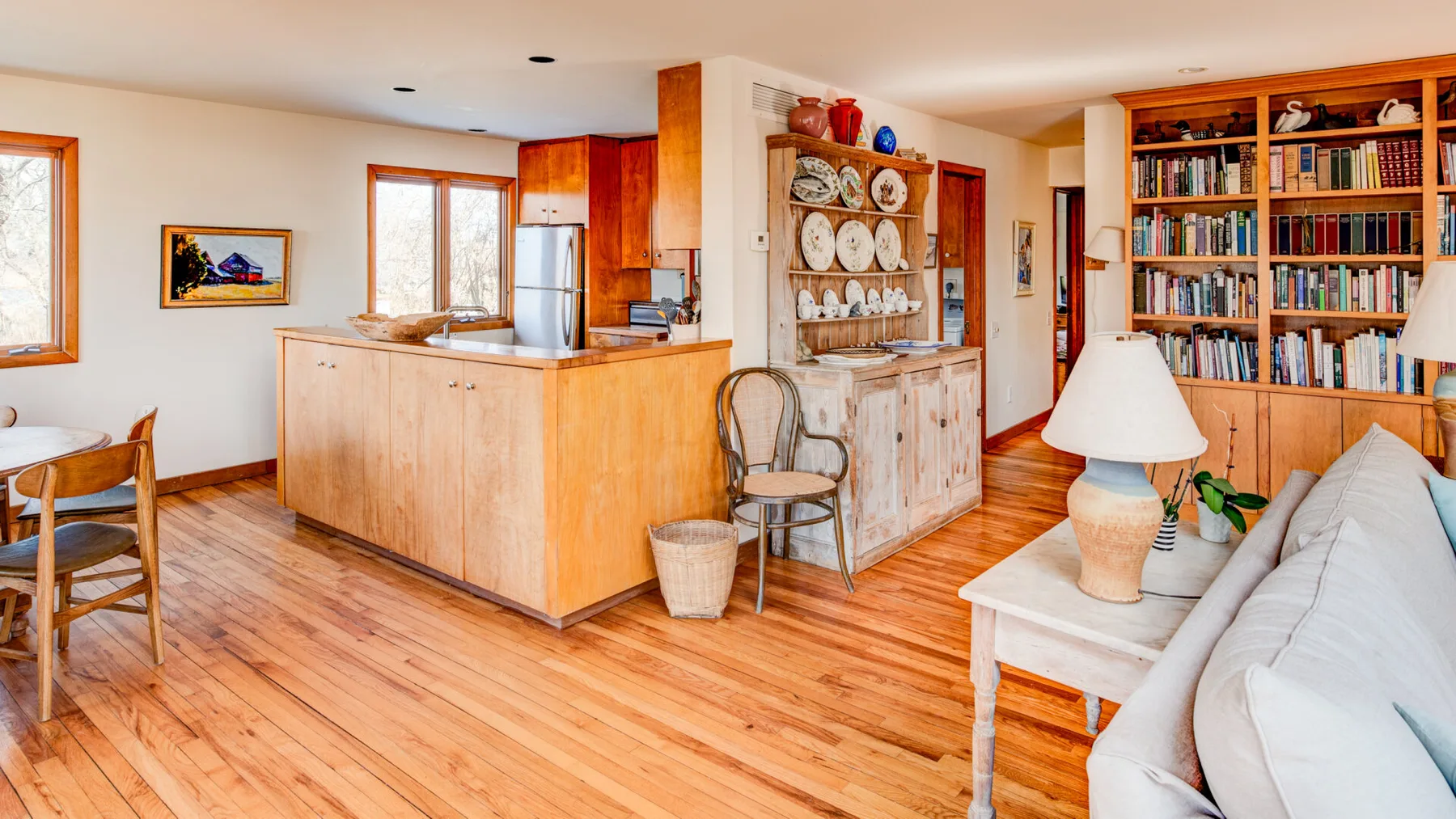 A bright open-plan living room and kitchen with a dining table and bookshelves.