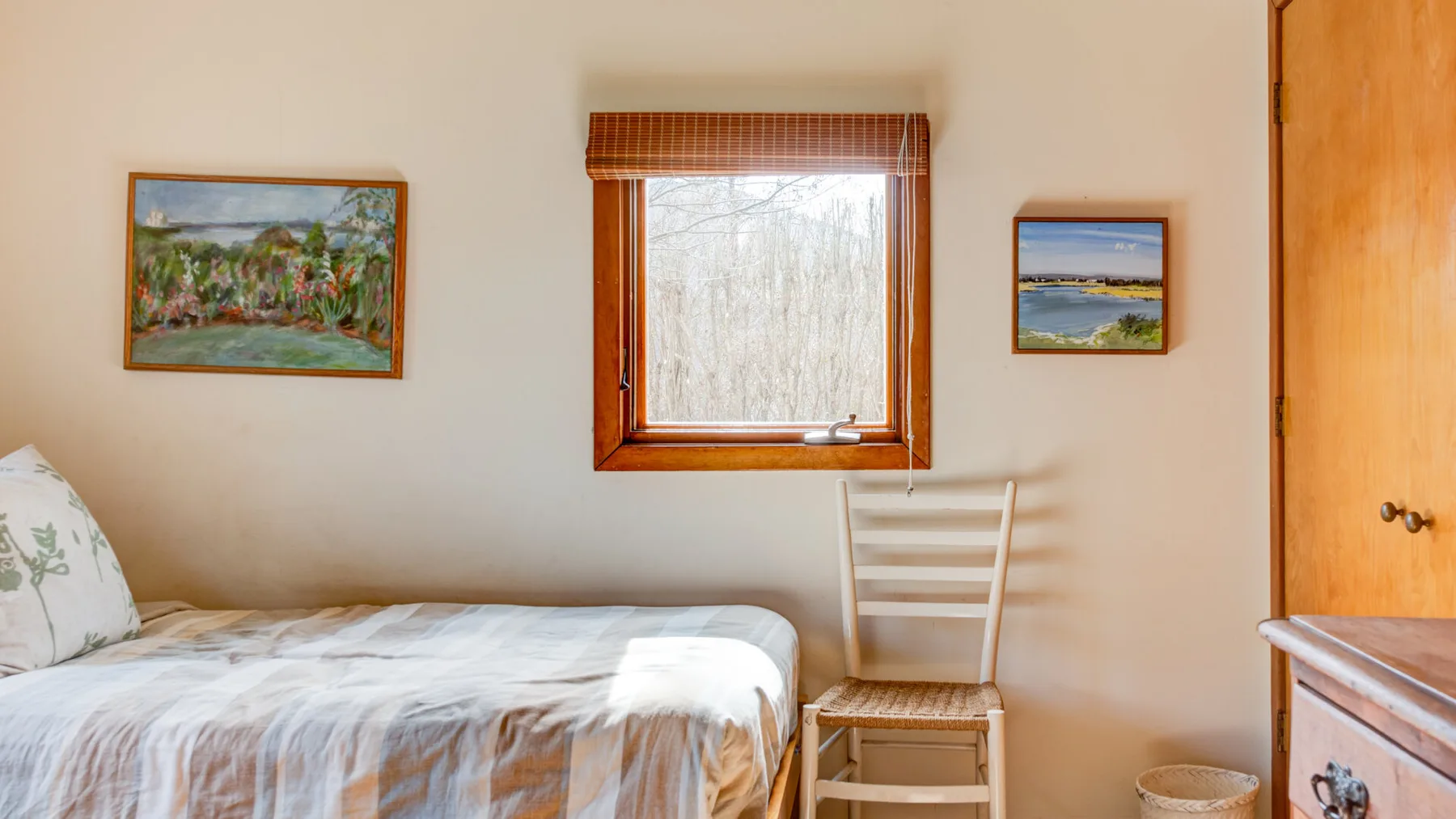 A bedroom with a bed, a wooden chair, and a window overlooking trees.