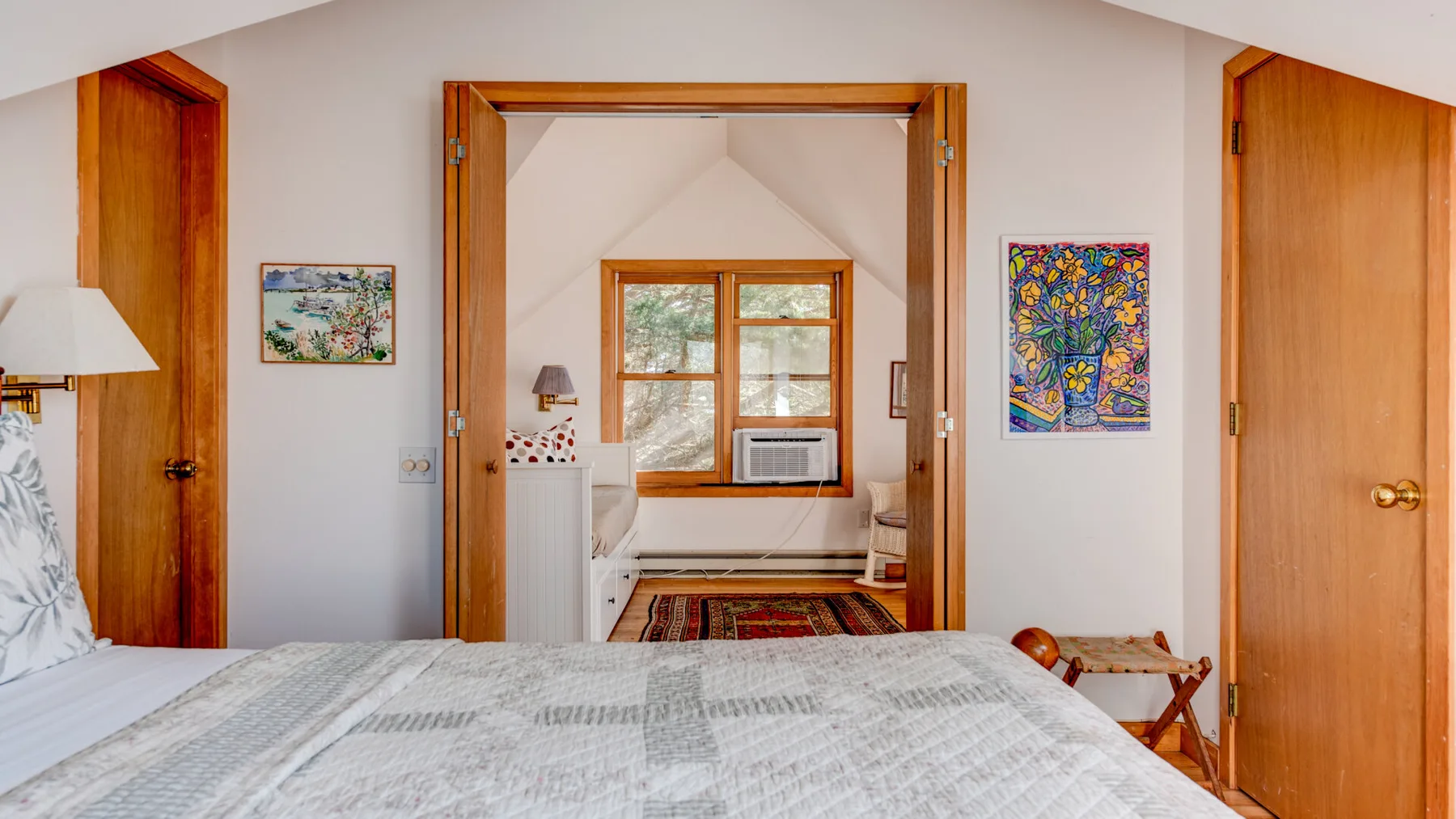 A bedroom with a bed, wooden doors, and an open view into an adjoining room.