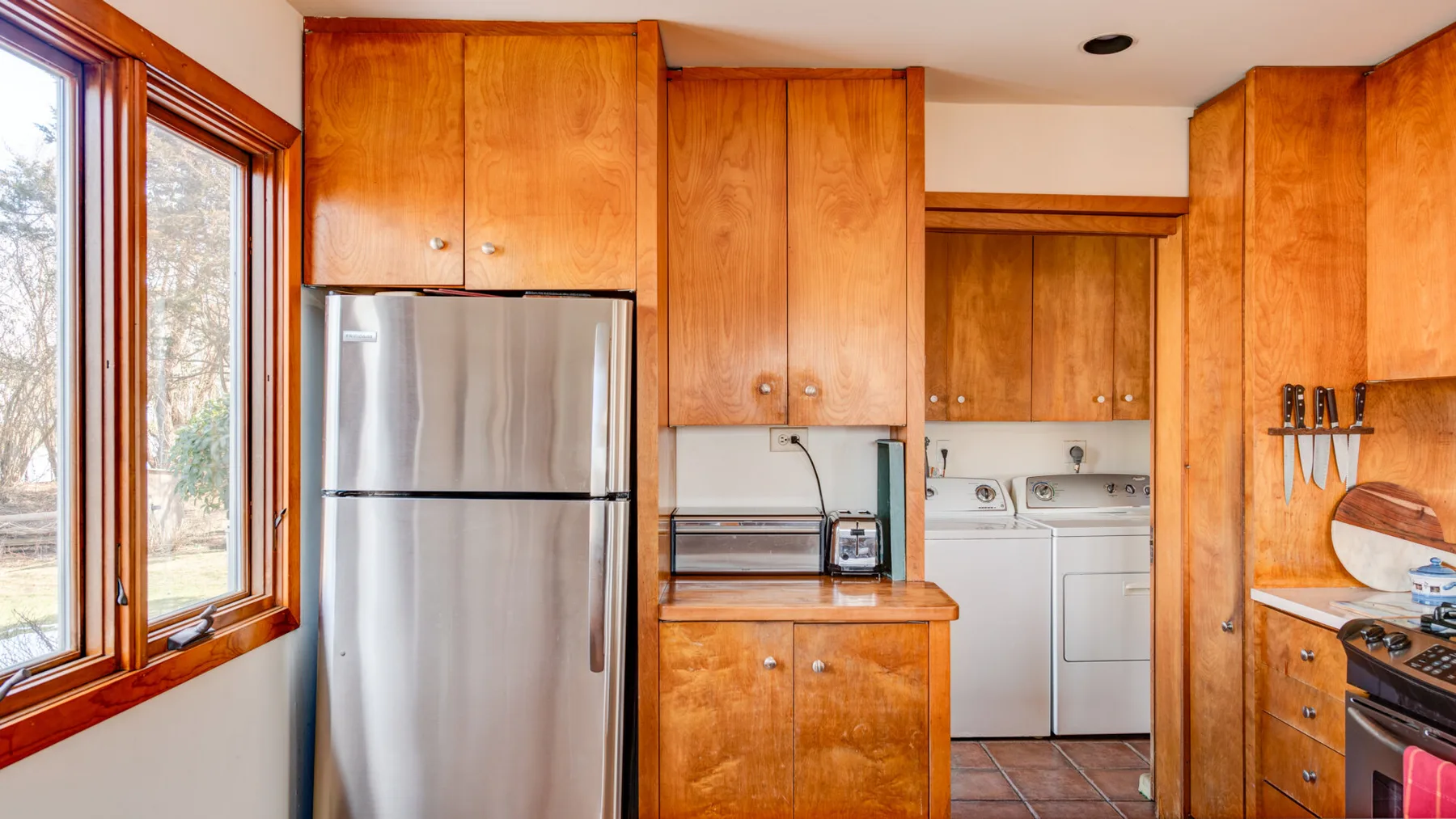 A kitchen with wooden cabinets, a refrigerator, and laundry appliances.