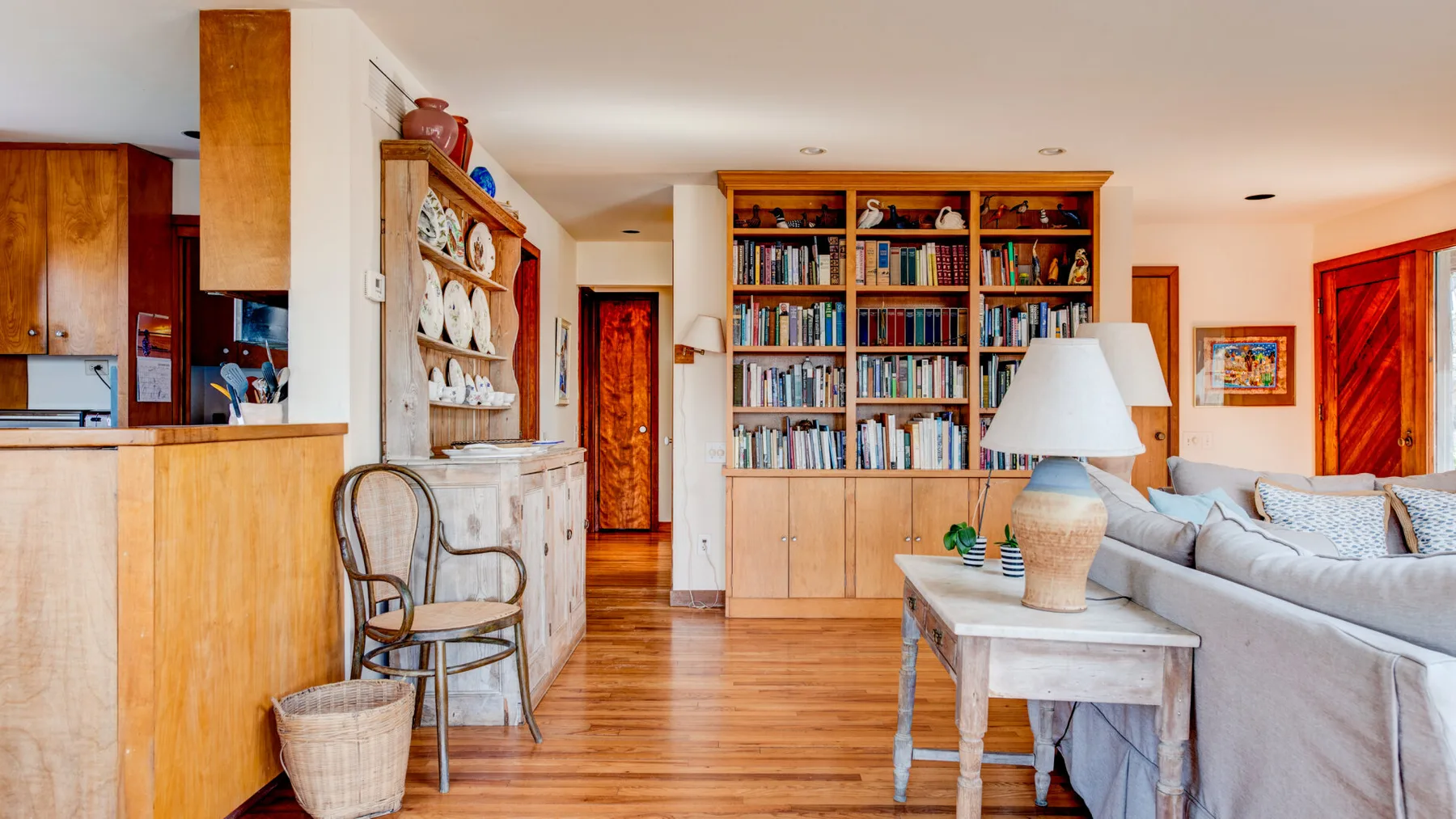 A living room with a large bookcase and seating beside a kitchen.