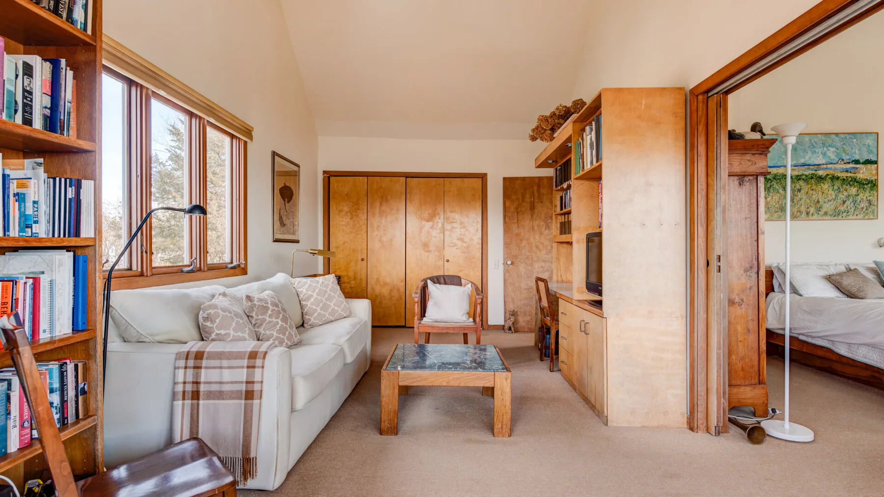 A living room with seating, a coffee table, and bookshelves beside large windows.