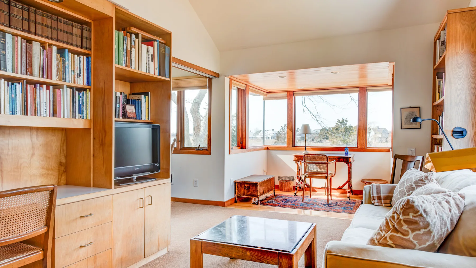 A living room with bookshelves, seating, and large windows.