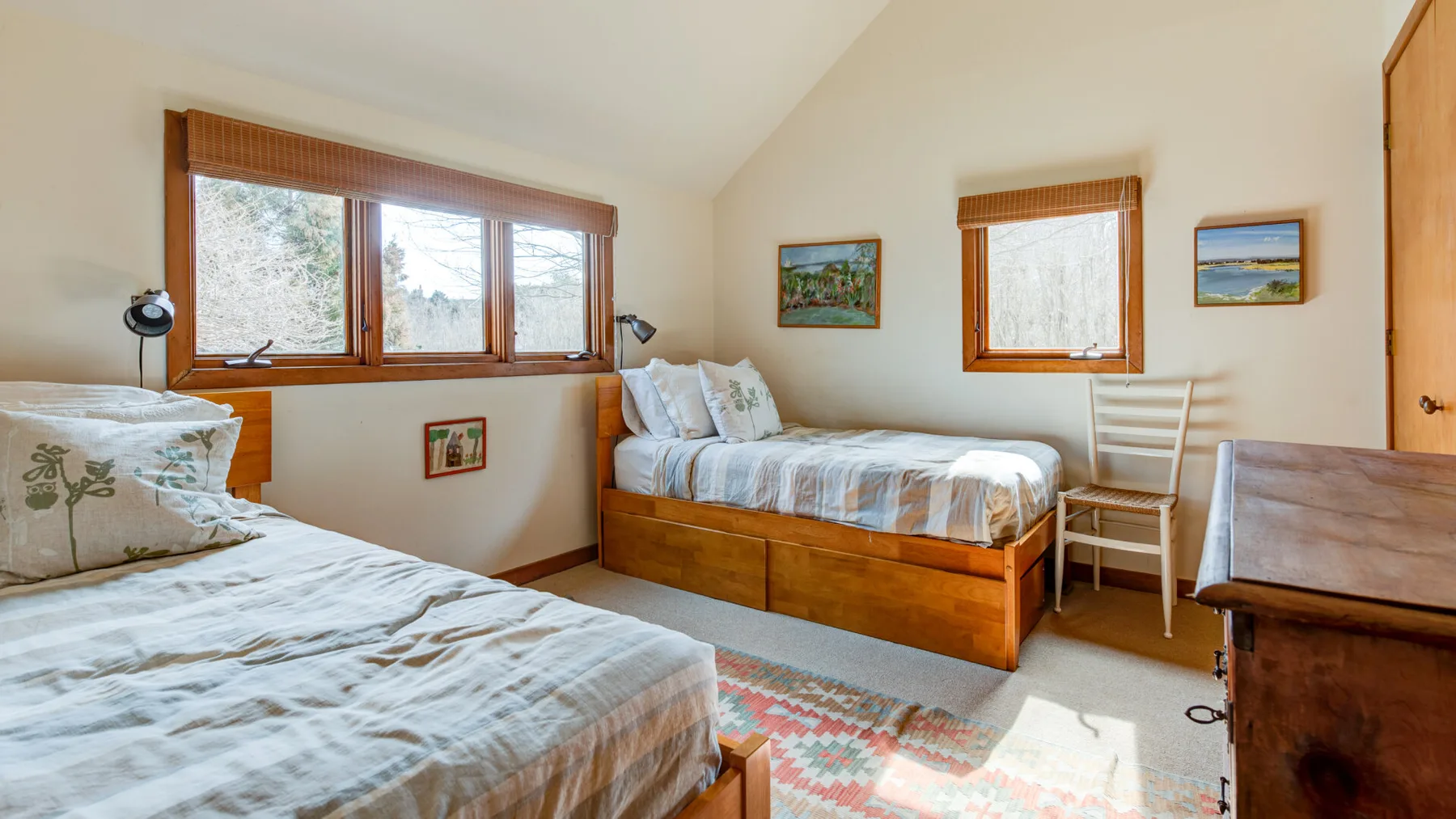 A bedroom with two beds, wood-framed windows, and a patterned rug.