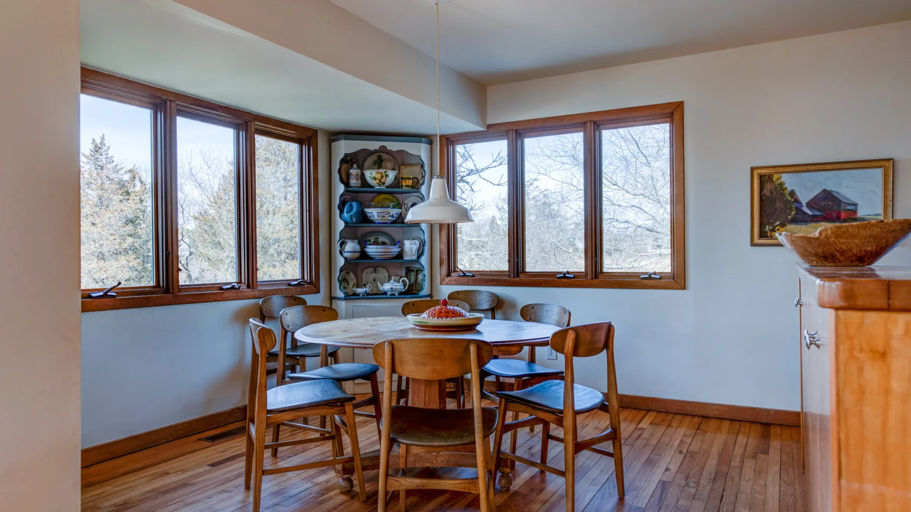 A dining area with a round wooden table and windows.